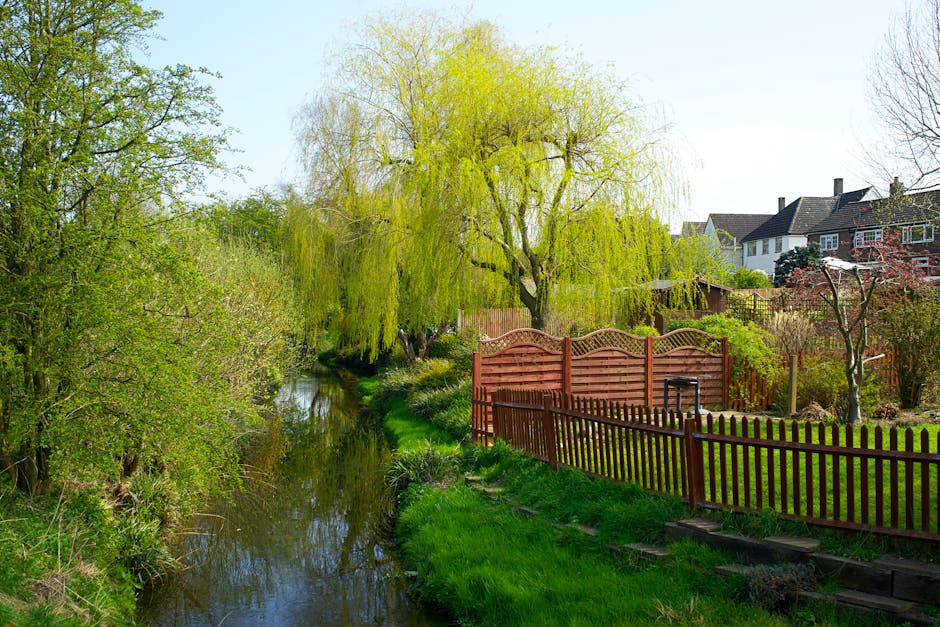 A scenic riverside garden featuring lush greenery and colorful flowerbeds along the edge of the River Cray in Crayford. The garden includes well-maintained grassy areas and a variety of trees with bro